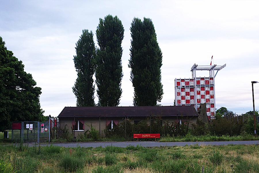 Ein einstöckiges Haus mit drei hohen Eiben auf dem Tempelhofer Feld.