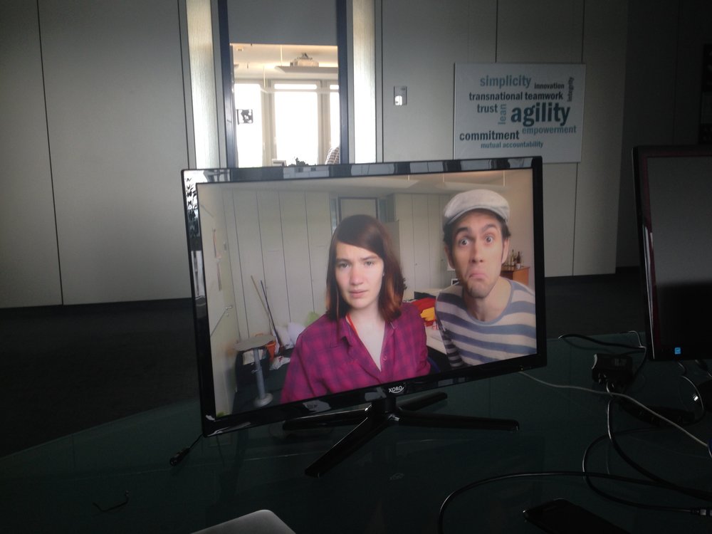 In einem Büro steht ein Flachbildschirm, von dem aus zwei Personen ratlos in die Kamera schauen.
